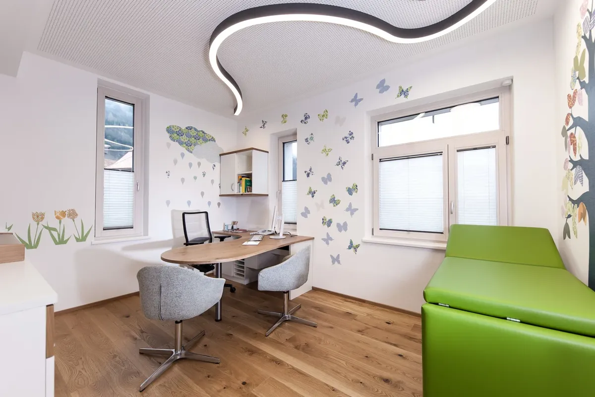 Behandlungszimmer mit Schmetterlingen an der Wand und grüner Liege